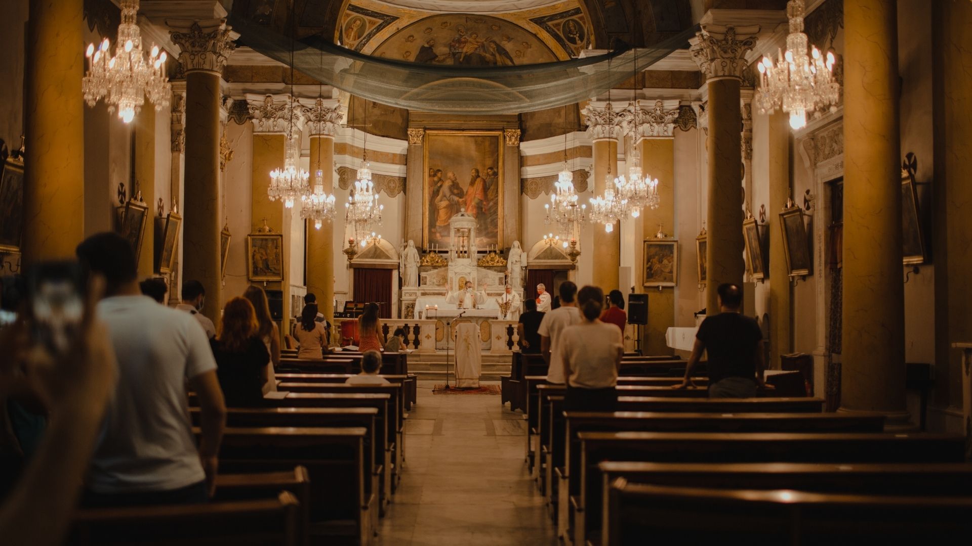 Cathedral sanctuary with chandeliers and worshippers attending an evening service